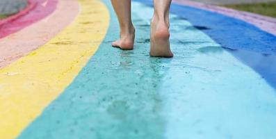 femmina piedi vicino su su a piedi nudi su bagnato asfalto disegnato arcobaleno a piedi sentiero dopo pioggia tra pozzanghere foto