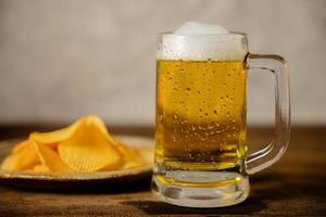 bicchiere di birra e piatto con poteto patatine fritte su tavolo. potabile birra a casa o bar foto