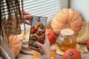 ragazza assunzione foto di zucche, autunno le foglie e teiera su un' finestra. ragazza Fotografare su Telefono rustico Halloween composizione. contento ringraziamento e Halloween