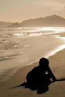 rio de janeiro, rj, brasile, 2021 - un' ragazzo nel silhouette giochi con sabbia a tramonto su barra spiaggia foto