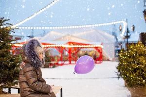 un' ragazza con un' Natale albero nel sua mani all'aperto nel caldo Abiti nel inverno a un' festivo mercato. Fata luci ghirlande decorato neve cittadina per il nuovo anno foto