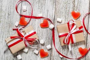 san valentino giorno caramella cuori marshmallows e scatola di i regali nel mestiere carta al di sopra di bianca di legno sfondo foto
