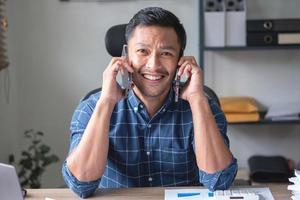 un' attività commerciale uomo chi è utilizzando Due mobile telefoni per comunicare con i clienti è difficile. il concetto è occupato. foto