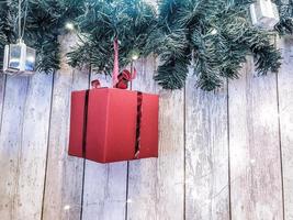 piccolo carino rosso festivo regalo scatole, Natale, nuovo anni decorazione su il sfondo di verde albero di Natale rami con aghi e raggiante ghirlande su di legno verticale tavole con cuciture foto