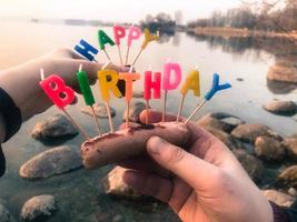 contento compleanno iscrizione fatto di vacanza candele nel il mani di un' uomo e un' donna di fronte il acqua di il oceano lago fiume foto