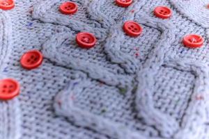 bellissimo struttura di un' morbido caldo naturale maglione con un' a maglia modello di filato e rosso piccolo il giro pulsanti per cucire. il sfondo foto