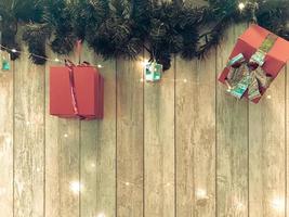 piccolo carino rosso festivo regalo scatole, Natale, nuovo anni decorazione su il sfondo di verde albero di Natale rami con aghi e raggiante ghirlande su di legno verticale tavole con cuciture foto
