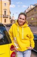 contento donna vicino un' giallo auto nel il città nel un' giallo giacca foto