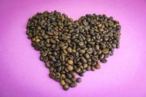 bellissimo struttura nel il forma di un' cuore a partire dal appena arrostito selezionato delizioso saturato Marrone naturale fragrante arabica e robusta caffè fagioli. copia spazio, piatto posizione, rosa viola sfondo foto