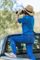 vicino su donna indossare cappello e hold binoculare nel erba campo foto