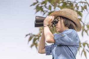 vicino su donna indossare cappello e hold binoculare nel erba campo foto