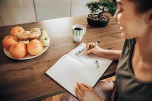 donna fabbricazione per fare elenco mentre godendo mattina caffè a casa foto