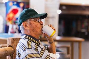 lato Visualizza dell'anziano uomo potabile birra mentre seduta nel un' sedia all'aperto. foto