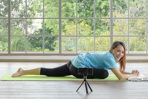 Candido contento Sorridi giovane asiatico donna allungamento Seguire in linea lezione a partire dal smartphone prima fare o praticante yoga a casa. giovane persone domestico vita concetto. selettivo messa a fuoco. foto