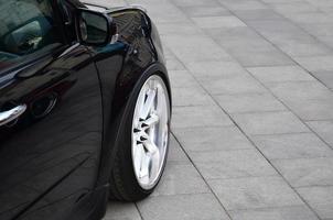 diagonale Visualizza di un' nero lucido auto con bianca ruote, quale sta su un' piazza di grigio piastrelle foto