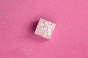 un' piccolo regalo scatola nel rosa con un' piccolo arco bugie su un' coperta di morbido e peloso leggero rosa vello tessuto. Imballaggio per un' regalo per il tuo bello fidanzata foto