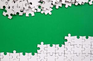 frammento di un' piegato bianca sega puzzle e un' mucchio di spettinato puzzle elementi contro il sfondo di un' verde superficie. struttura foto con spazio per testo