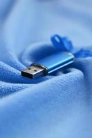 brillante blu USB veloce memoria carta con un' blu arco bugie su un' coperta di morbido e peloso leggero blu vello tessuto con un' lotto di sollievo pieghe. memoria Conservazione dispositivo nel Da donna design foto