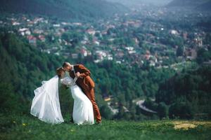 contento elegante sposa e sposo in esecuzione e avendo divertimento nel montagne su estate soleggiato giorno. bellissima sposini coppia ridendo, vero sentimenti. emotivo romantico momento. foto