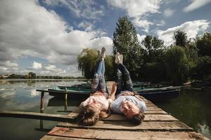 Perfetto Data. bellissimo giovane coppia e sorridente mentre dire bugie su il molo. contento giovane uomo e donna ridendo mentre dire bugie su di legno molo vicino acqua foto