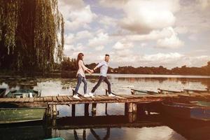 contento giovane coppia all'aperto. giovane amore coppia in esecuzione lungo un' di legno ponte Tenere mani. foto