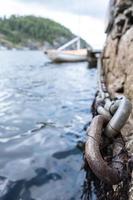 ferro catena su vecchio pietra molo, mare onde e ormeggiato barca a vela e roccioso riva su di messa a fuoco. parte inferiore Visualizza. foto