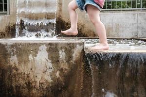 bambino corre a piedi nudi allegramente attraverso chiaro in esecuzione acqua nel il modulo di un' cascata. foto