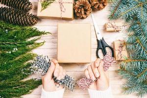 donna involucro Natale presente , ragazza prepara natale i regali con abete albero e pino cono. mano artigianale regalo su di legno sfondo con Natale arredamento. superiore Visualizza, copia spazio. tonica foto