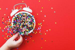 del bambino mani hold allarme orologio con sparpagliato paillettes su un' rosso sfondo. Natale, celebrazione concetto foto