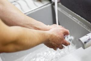 un' uomo lavaggi il suo mani con sapone sotto il rubinetto sotto in esecuzione acqua avvicinamento. Salute, e igiene concetto. foto