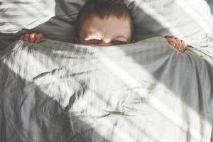 ragazzo dormire nel il letto. bambino bugie su cuscino e coperture il suo viso con un' coperta foto