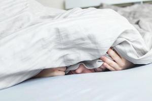 ragazzo nel il letto nel il mattina. bambino bugie e coperture il suo viso con un' coperta foto