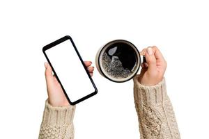 Natale in linea acquisti. femmina mani nel maglione toccare schermo mobile Telefono con tazza di caffè. donna digitando su mobile Telefono isolato su bianca sfondo foto