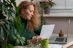 un' mezza età donna d'affari lavori a un' scrivania, fa Appunti nel un' computer portatile, e controlli il dati su sua Telefono. attività commerciale, in linea attività commerciale, opera nel il ufficio foto