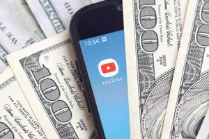 Kharkov, Ucraina - Maggio 3, 2022 smartphone schermo con Youtube App e lotto di centinaio dollaro fatture. attività commerciale e sociale networking concetto foto