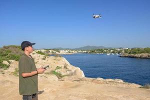 contento adolescente ragazzo, volante fuco su mediterraneo costa, contro blu cielo durante soleggiato giorno Spagna, baleari isole foto