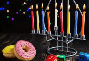 ebraico vacanza hanukkah sfondo. un' tradizionale piatto è dolce ciambelle. hanukkah tavolo ambientazione candeliere con candele e Filatura cime su nero sfondo. illuminazione chanukah candele. copia spazio foto