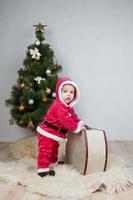 piccolo ragazzo in costume da Babbo Natale gioca in studio bianco foto