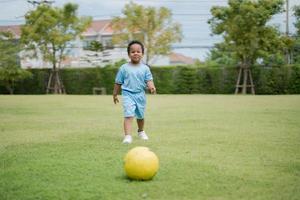 carino poco ragazzo con calcio palla nel il parco su un' soleggiato giorno. foto