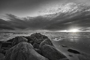 tramonto su il spiaggia nel Danimarca prese nel nero e bianca. pietra frangiflutti