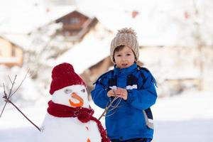 felice bel bambino edificio pupazzo di neve in giardino, inverno foto