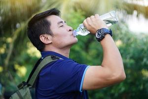 bello asiatico uomo viaggiatore detiene bottiglia di potabile acqua per bevanda all'aperto. concetto ,potabile acqua per Salute, salutare stile di vita.spegnere sete, ridurre fatica, rinfresca corpo. foto