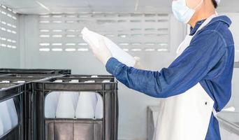 giovane uomo lavoratore o qualità ispettore nel abbigliamento da lavoro e con un' protettivo maschera su il suo viso Lavorando nel controllo in bottiglia potabile acqua nel bevanda acqua fabbrica prima spedizione.bere acqua attività commerciale foto