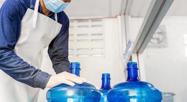 ispezione qualità controllo. uomo lavoratore nel abbigliamento da lavoro e con un' protettivo maschera su il suo viso Lavorando nel un' bevanda acqua fabbrica controllo acqua galloni prima spedizione. foto