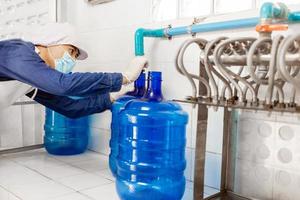 uomo lavoratore nel abbigliamento da lavoro e con un' protettivo maschera su il suo viso Lavorando produce potabile acqua nel un' pulito potabile acqua fabbrica. pulito potabile acqua produzione linea foto