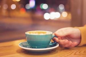 uomo mano con tazza di caffè nel un' bar su un' sfondo di città luci dietro a finestra. tonica foto. foto