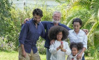 Multi etnico caucasico - africano famiglia gruppo rilassare assunzione un' camminare e preparare per celebrazione insieme su vacanza a Giardino dietro la casa Casa con contento sorridente viso. selettivo messa a fuoco. foto