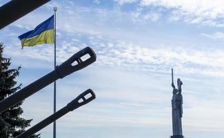 il ucraino bandiera svolazzanti nel il vento, vicino il famoso statua di il patria. il maggiore nazionale bandiera di Ucraina nel il blu cielo. bellissimo autunno paesaggio. Ucraina, kyiv - ottobre 9, 2022. foto