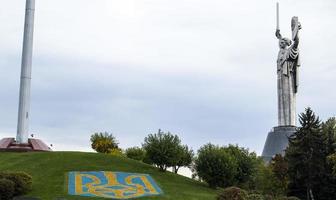 statua di il patria contro il blu cielo. cappotto di braccia di Ucraina su il prato, foderato con blu e giallo pietre. il tridente, il ufficiale simbolo di il stato. Ucraina, kyiv - ottobre 08, 2022. foto