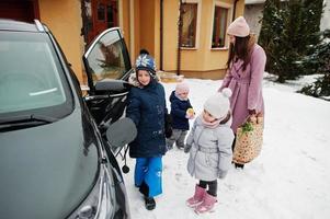 giovane donna con bambini tiene borse ecologiche e carica un'auto elettrica nel cortile di casa sua. foto